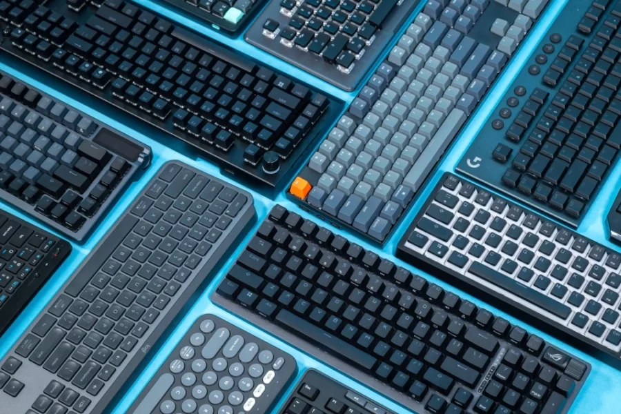 A variety of modern mechanical and wireless keyboards arranged on a blue background, showcasing some of the best keyboards for programming in 2025, including compact layouts, ergonomic designs, and models with customizable keys and RGB lighting.