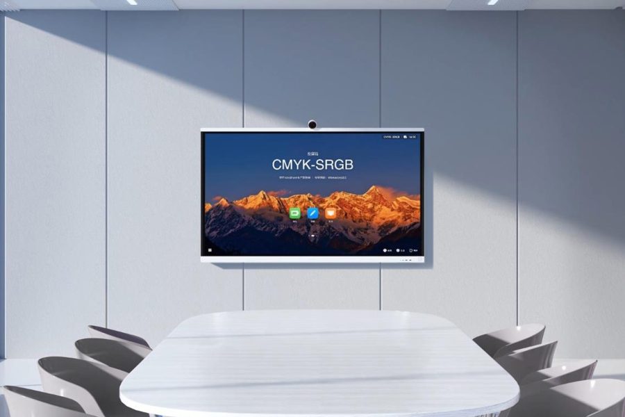 Essential Video Conferencing Upgrades for Large Meeting Rooms: A sleek, wall-mounted Huawei IdeaHub S2 dominates the view above a large, modern white conference table surrounded by grey chairs in a well-lit meeting space. The display shows a vibrant image of snow-capped mountains under a warm sky and the text "CMYK-SRGB," suggesting advanced color management capabilities for professional video conferencing.