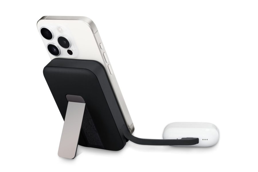 A black magnetic wireless power bank with a silver kickstand attached to the back of a silver iPhone, which is connected by a short black cable to white AirPods Pro charging case.
