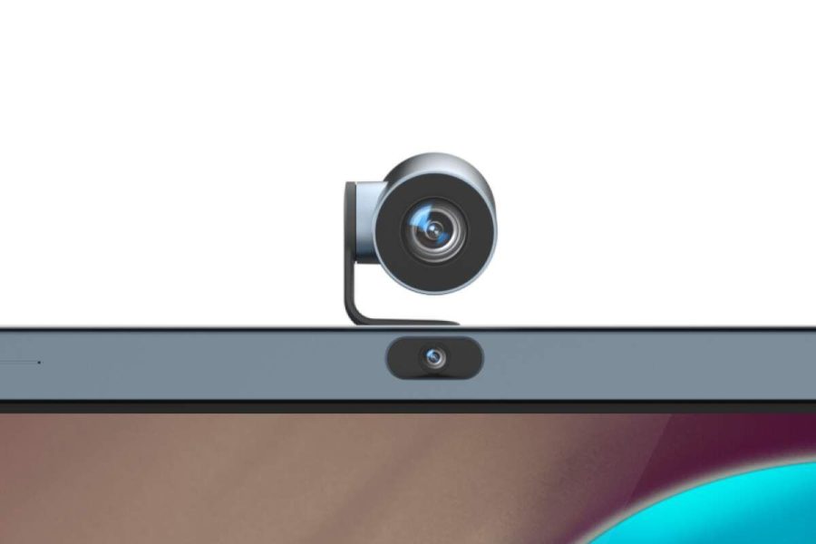 A black webcam is clipped to the top center of a laptop screen, with the laptop's built-in webcam visible directly below it. The screen displays a colorful, abstract background.