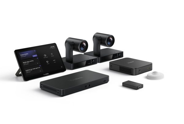 A professional setup of Yealink video conferencing equipment arranged on a white surface. From left to right, there's a black tablet displaying what appears to be a meeting schedule or interface. Behind it are two identical, sleek black cameras with cylindrical lenses mounted on rectangular bases. In front of the cameras are two rectangular black devices, one slightly larger than the other, both with the Yealink logo. To the far right, there's a small, rectangular black dongle and a small, white, circular device, likely a microphone or speaker.