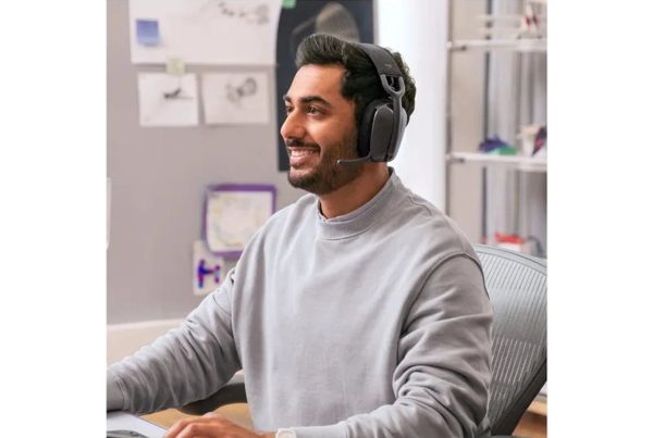 Man wearing a black wireless headset with a boom mic during a video call at work.