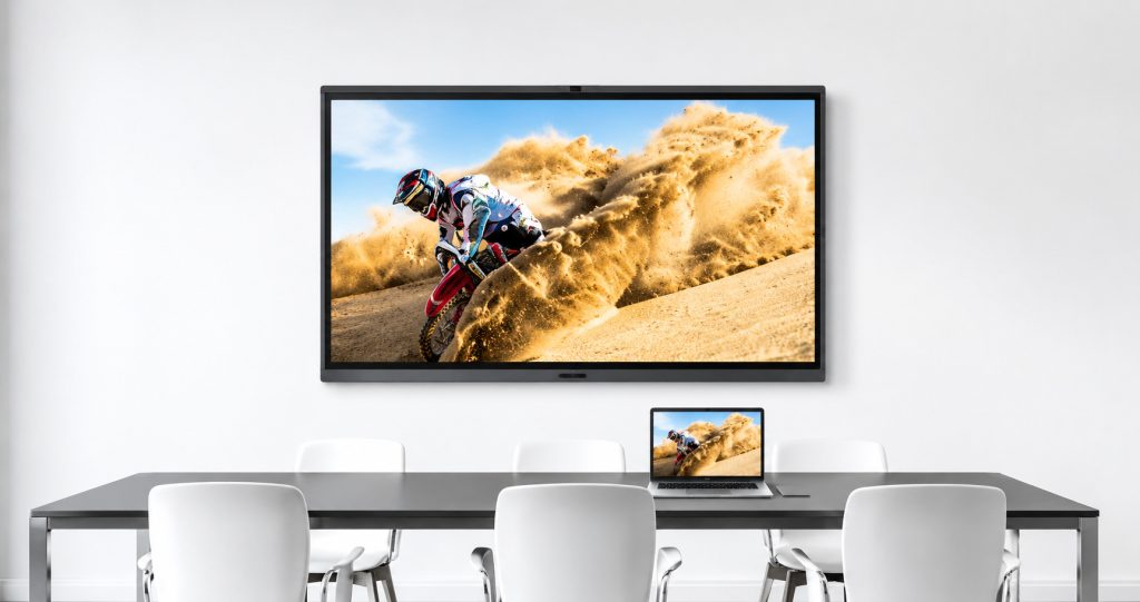 MAXHUB interactive display wall-mounted in a modern conference room with a motocross rider image mirrored on a laptop screen placed on the table
