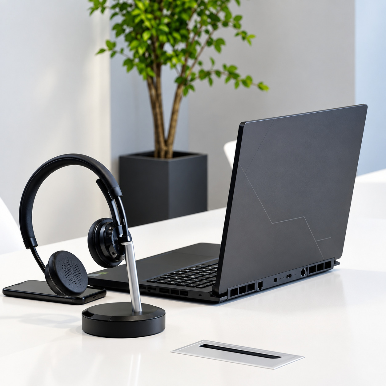 VT X300 BT dual-ear Bluetooth wireless headset resting on its charging base alongside an open black laptop and smartphone on a modern white office desk
