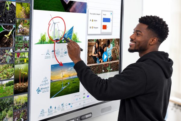 A smiling man using a stylus to write and interact with an interactive smart display board showing an educational lesson on renewable energy.