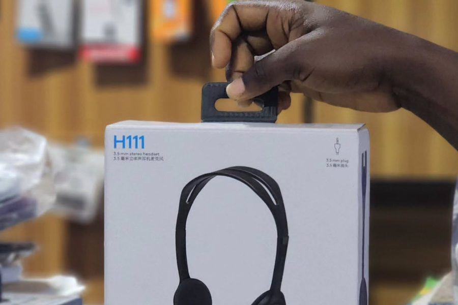 A hand holding the retail packaging box of a Logitech H111 3.5mm stereo headset in a store setting.